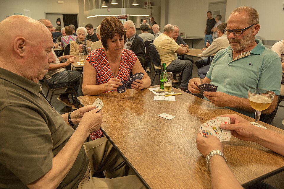 Four players around a club table holding cards during an evening of Belote