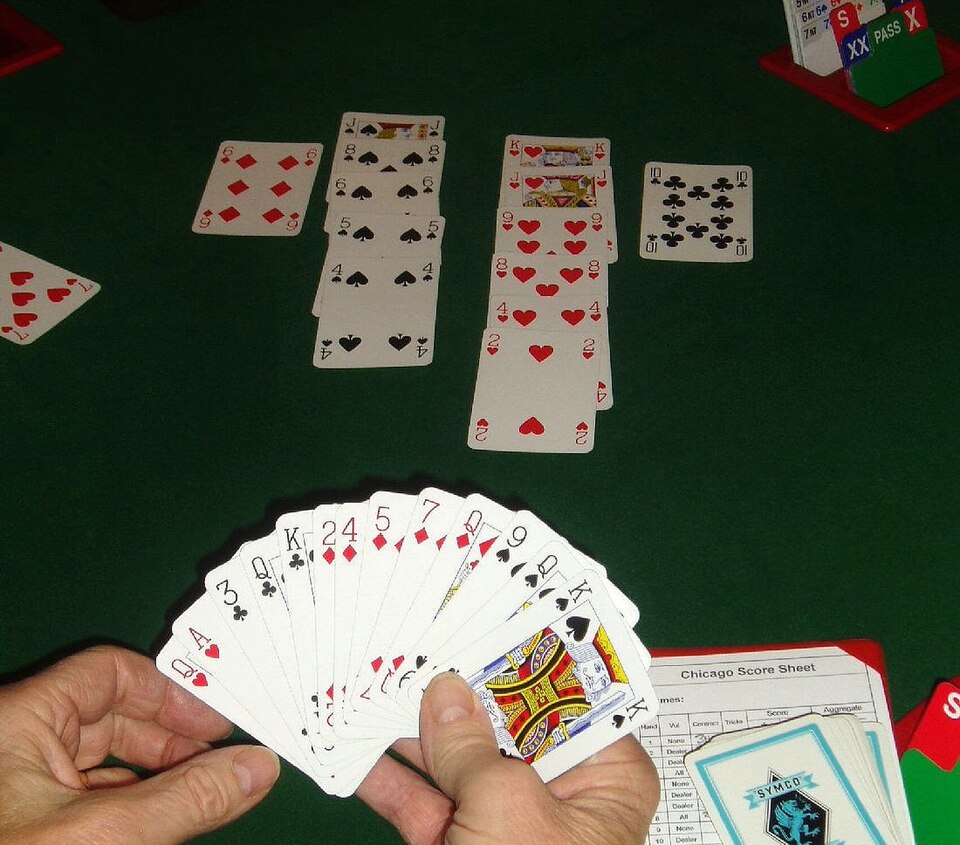 A player holds a fan of standard playing cards above green felt, with finished tricks laid out in rows