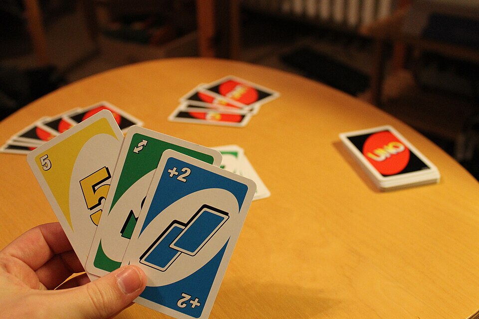A hand of Uno cards with a yellow 5, a green Reverse and a blue Draw Two above a wooden table